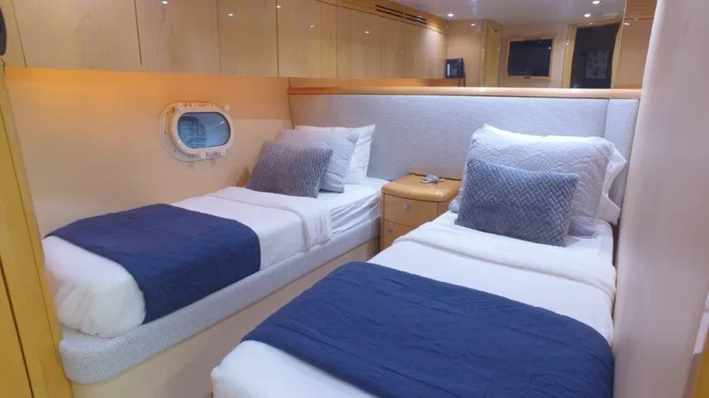 Slide: The Image of 2006 Hatteras Enclosed Bridge cabin with twin beds, blue accents, and porthole window. - 14