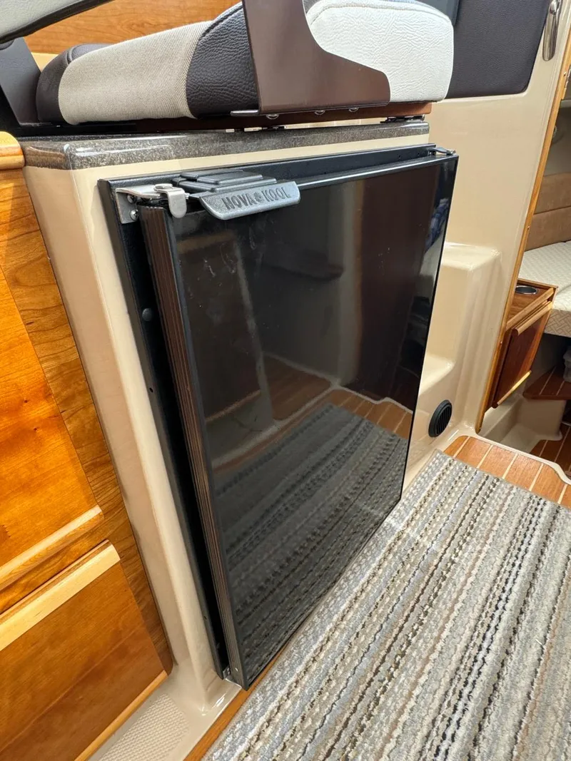 Slide: The Image of 2017 Cutwater C28 interior with compact black fridge and wooden cabinetry. - 34