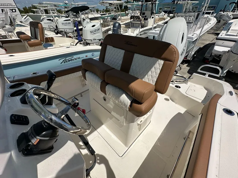 Slide: The Image of 2024 Pioneer 222 Sport Fish boat interior with seating and cooler, displayed at a marina. - 6