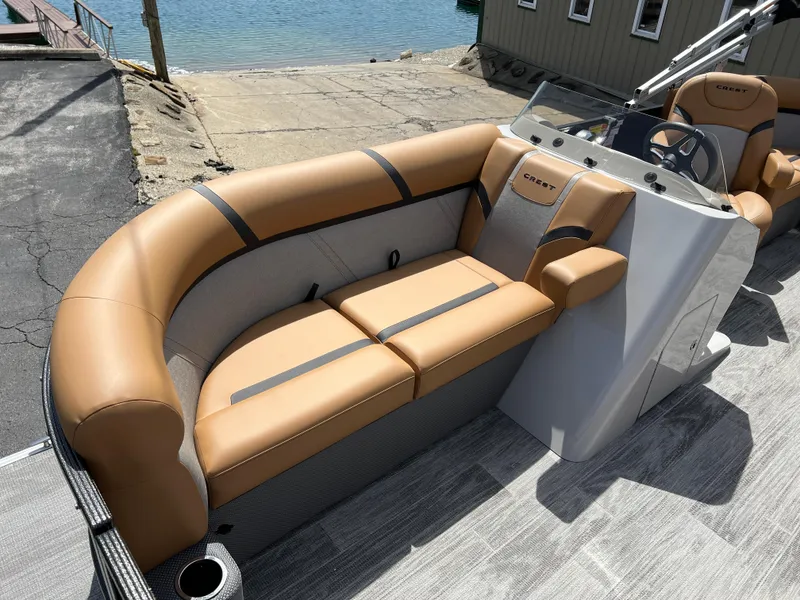 Slide: The Image of 2024 Crest Classic LX 220 boat interior with tan and gray seating, docked by the water. - 7