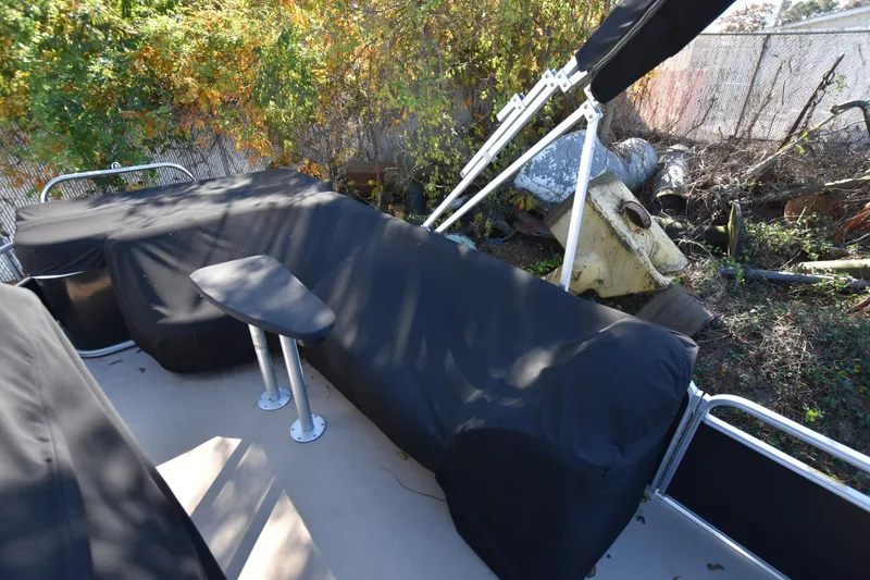 Slide: The Image of 2014 AquaPatio 240 boat interior with covered seating and table, near foliage and debris. - 8