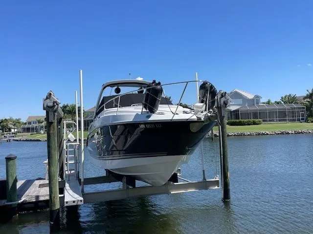 Slide: The Image of 2019 Monterey 295 boat on lift, docked by waterfront homes under clear blue sky. - 2