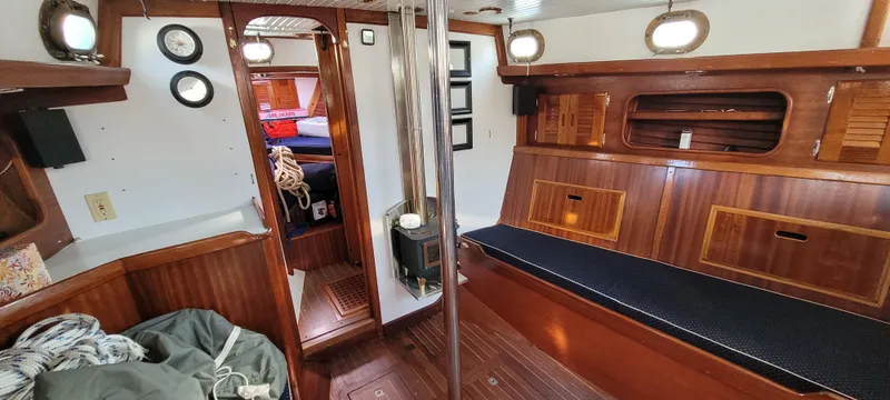 Slide: The Image of 1976 Westsail Ketch interior with wooden finish, cozy seating, and nautical decor. - 46