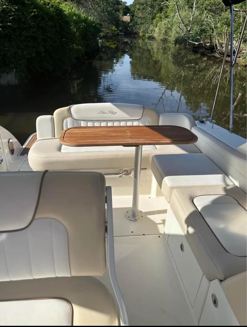 Slide: The Image of 2013 Sea Ray Sundancer boat interior with seating and wooden table, surrounded by lush greenery. - 12