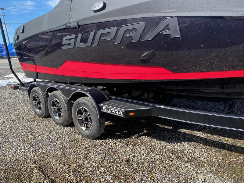 Slide: The Image of 2021 Supra SE boat on a triple-axle trailer with a black and red design. - 3