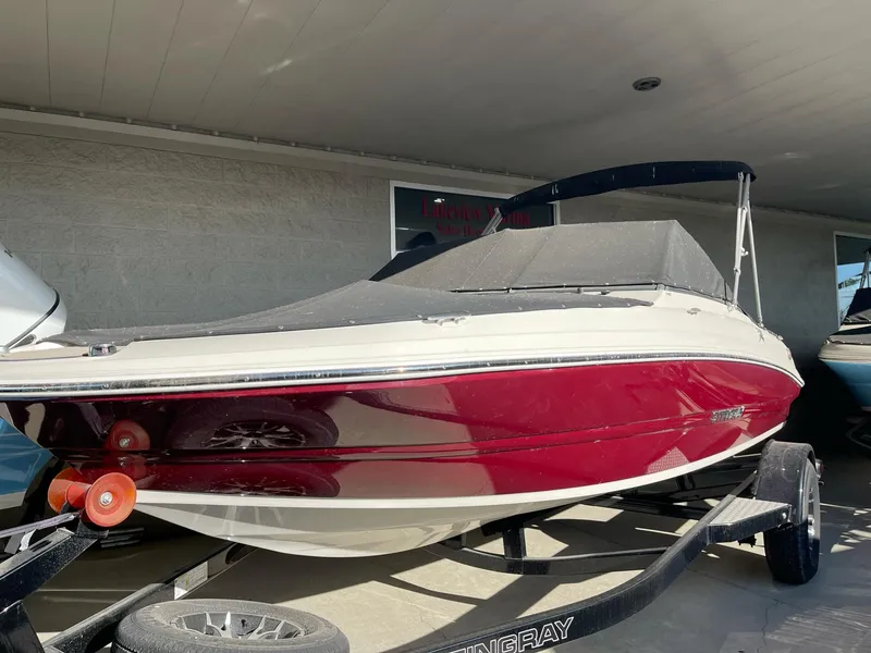 Slide: The Image of 2024 Stingray 191 DC boat with red hull on trailer, under a covered area. - 30