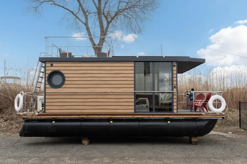 Slide: The Image of Waterlodge Apart M 2024 houseboat with wooden exterior and rooftop deck, docked on a sunny day. - 2