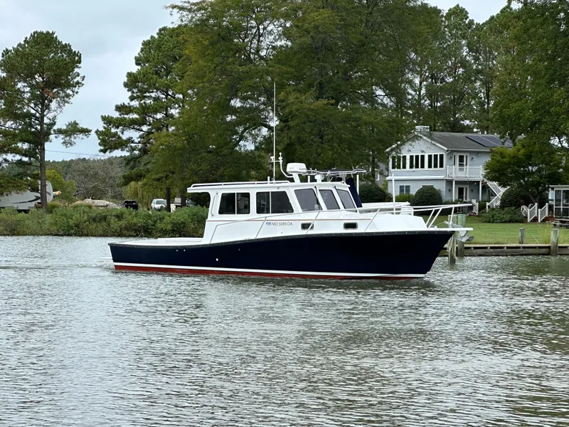 Slide: The Image of 2016 Custom Broad Creek 32 Downeast boat on calm water near a house and trees. - 4