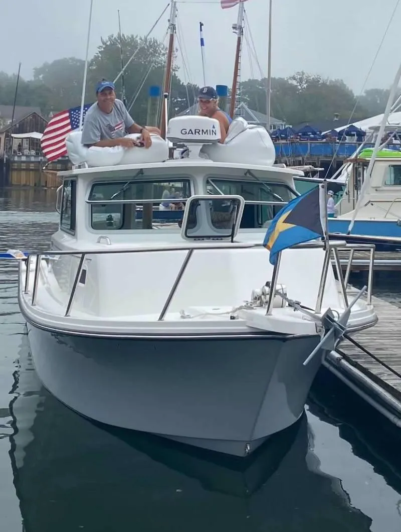 Slide: The Image of 2020 Parker 2520 XL Deep Vee Sport Cabin boat docked with flags and two people onboard. - 2