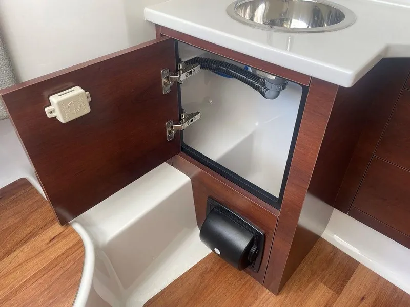 Slide: The Image of 2024 Chaparral 280 OSX boat interior, open cabinet with sink and wood finish. - 41