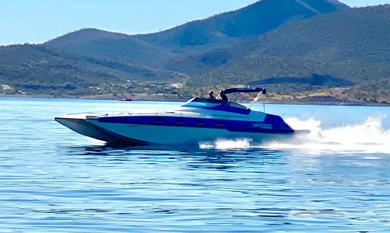 Slide: The Image of 1988 Warlock 37 Cat Cruiser speeding on a lake with mountainous background. - 2