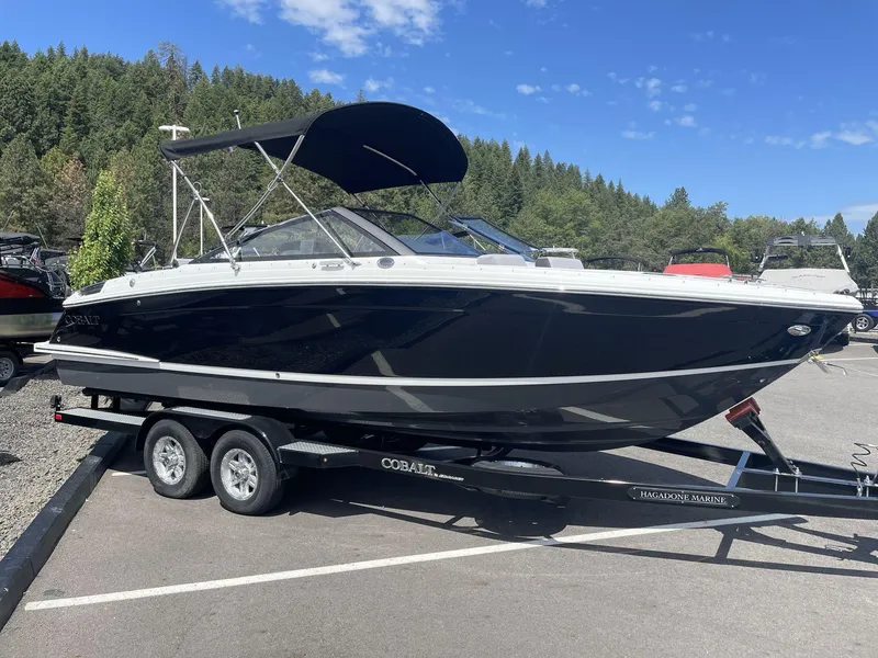Slide: The Image of 2024 Cobalt R4 boat on trailer, parked outdoors with forest background. - 2