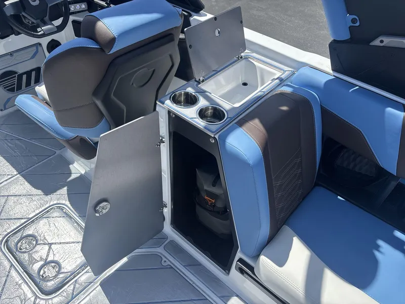 Slide: The Image of 2024 Malibu 25LSV boat interior with blue and brown seating, open storage, and cup holders. - 15