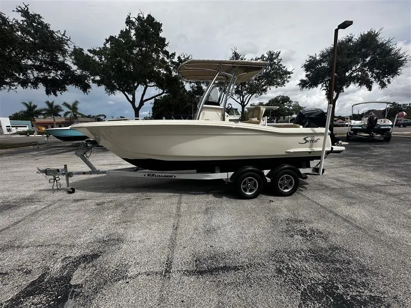 The Image of 2021 Scout 215 XSF boat on trailer in parking lot, overcast sky. - 0