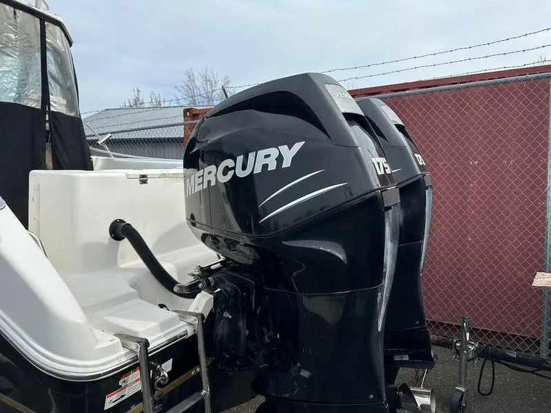Slide: The Image of 2012 Striper 2601 Walkaround with dual Mercury 175 outboard engines, parked near a chain-link fence. - 14