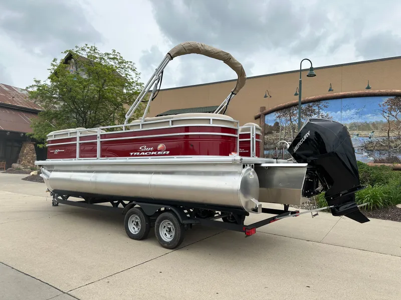 Slide: The Image of 2024 Sun Tracker Party Barge 22 XP3 pontoon boat on trailer, red and silver, outdoor setting. - 2