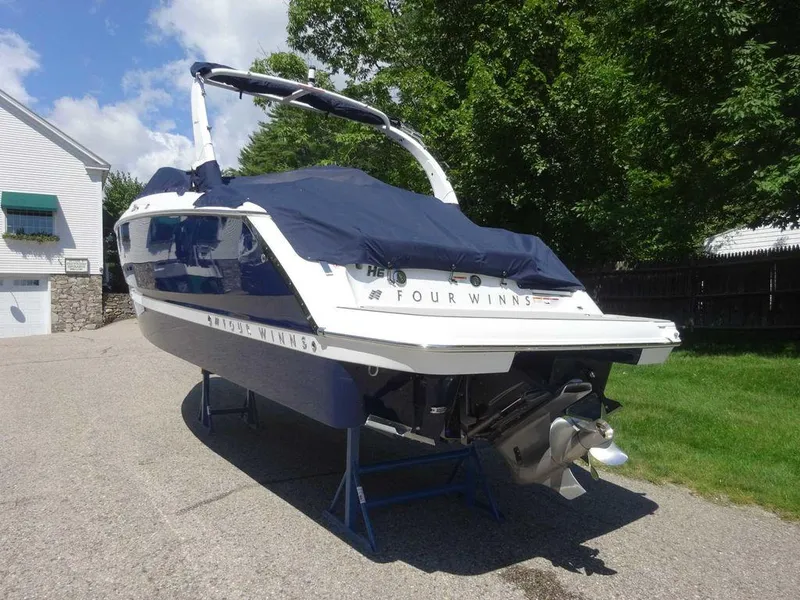Slide: The Image of 2024 Four Winns H6 boat with cover, parked on driveway, surrounded by trees. - 23
