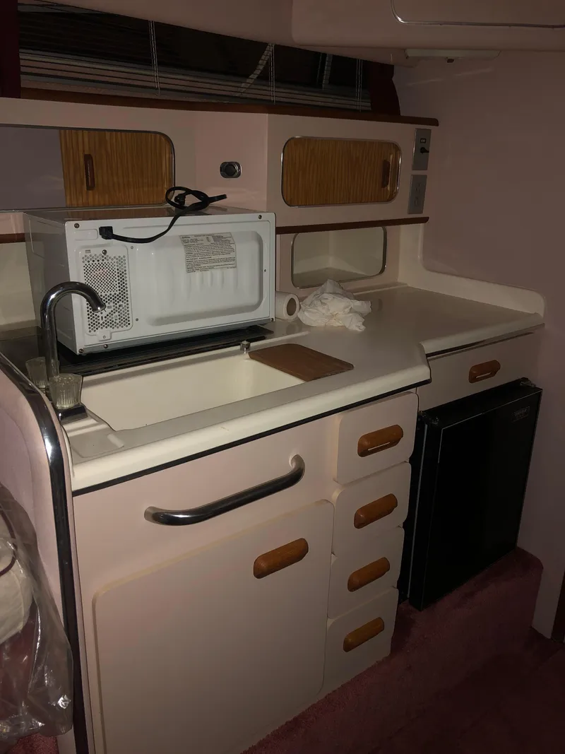 Slide: The Image of 1989 Sea Ray 280 Sundancer boat kitchenette with microwave, sink, and storage cabinets. - 13