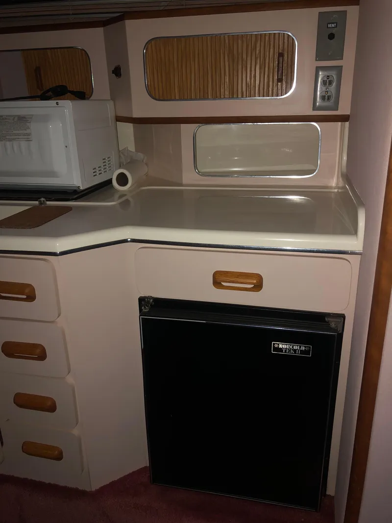 Slide: The Image of 1989 Sea Ray 280 Sundancer kitchenette with microwave, fridge, and storage cabinets. - 17