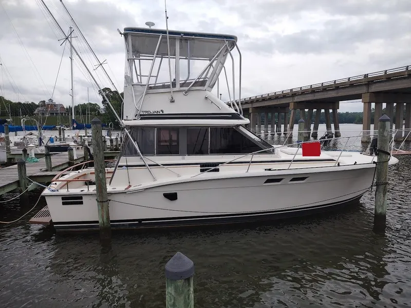 Slide: The Image of 1988 Trojan F32 Sedan boat docked near a bridge on a cloudy day. - 0