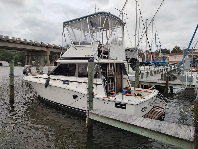 Slide: The Image of 1988 Trojan F32 Sedan boat docked at marina, overcast sky, bridge in background. - 2