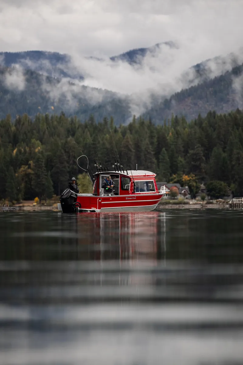 Slide: The Image of Red 2024 Spartan 240 Maximus Pro boat on a serene lake with forested mountains. - 5