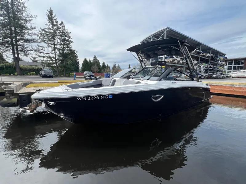 Slide: The Image of 2024 Cobalt R6 Surf boat docked on calm water, surrounded by trees and marina. - 2