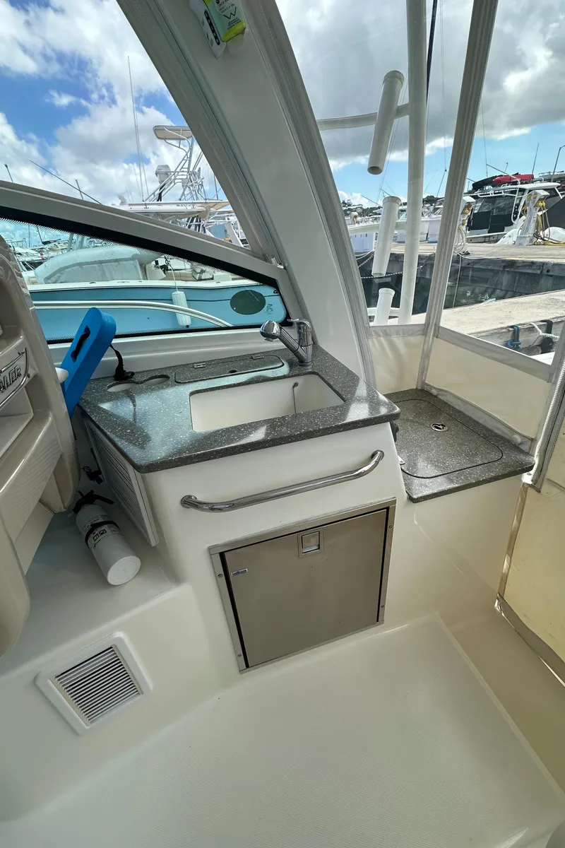 Slide: The Image of 2015 Boston Whaler 345 Conquest interior with sink and storage, docked under a cloudy sky. - 6