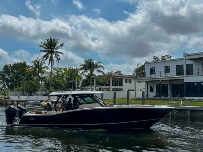 Slide: The Image of 2023 Scout 400 LXF boat cruising near waterfront homes with palm trees. - 3