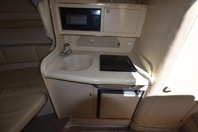 Slide: The Image of Compact kitchen area in a 1998 Sea Ray 270 Sundancer boat with sink, stove, microwave, and mini-fridge. - 16