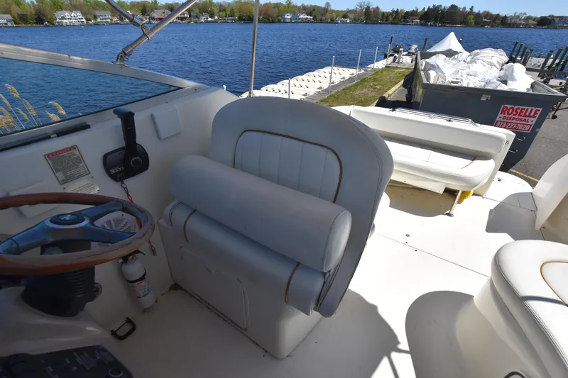 Slide: The Image of 1998 Sea Ray 270 Sundancer boat interior with helm and seating, docked by a lake. - 9