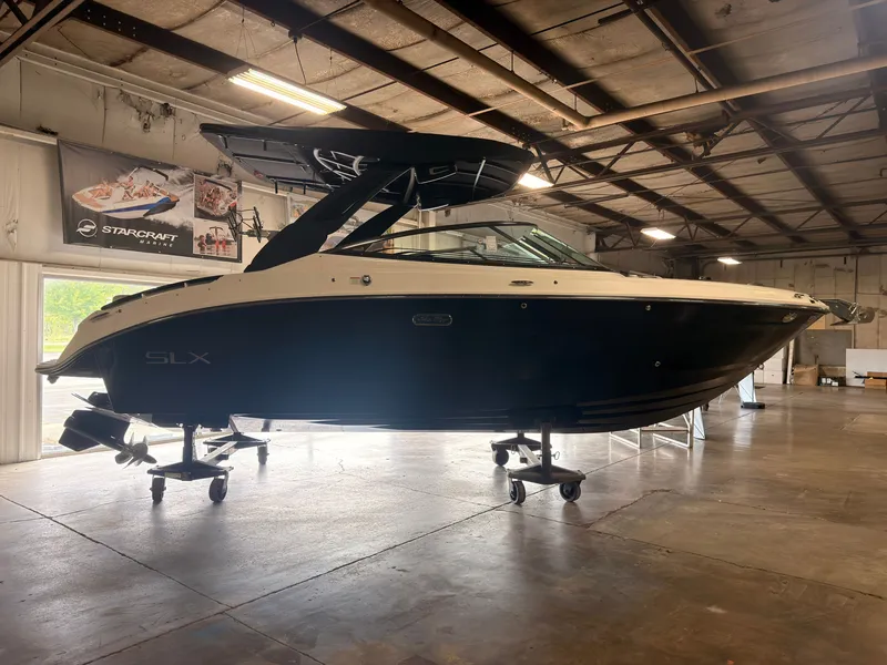 Slide: The Image of A 2024 Sea Ray SLX 260 Surf boat is on stands in a warehouse. - 1