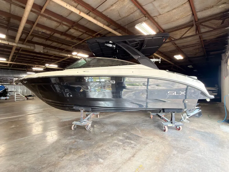 Slide: The Image of A 2024 Sea Ray SLX 260 Surf boat is on dollies in a warehouse. - 2