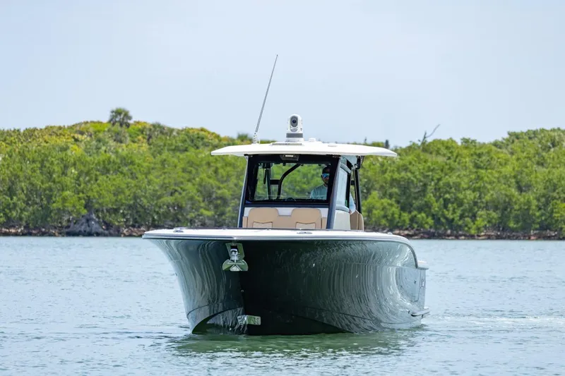 Slide: The Image of 2022 Scout 330 LXF boat cruising on calm water with lush greenery in the background. - 2