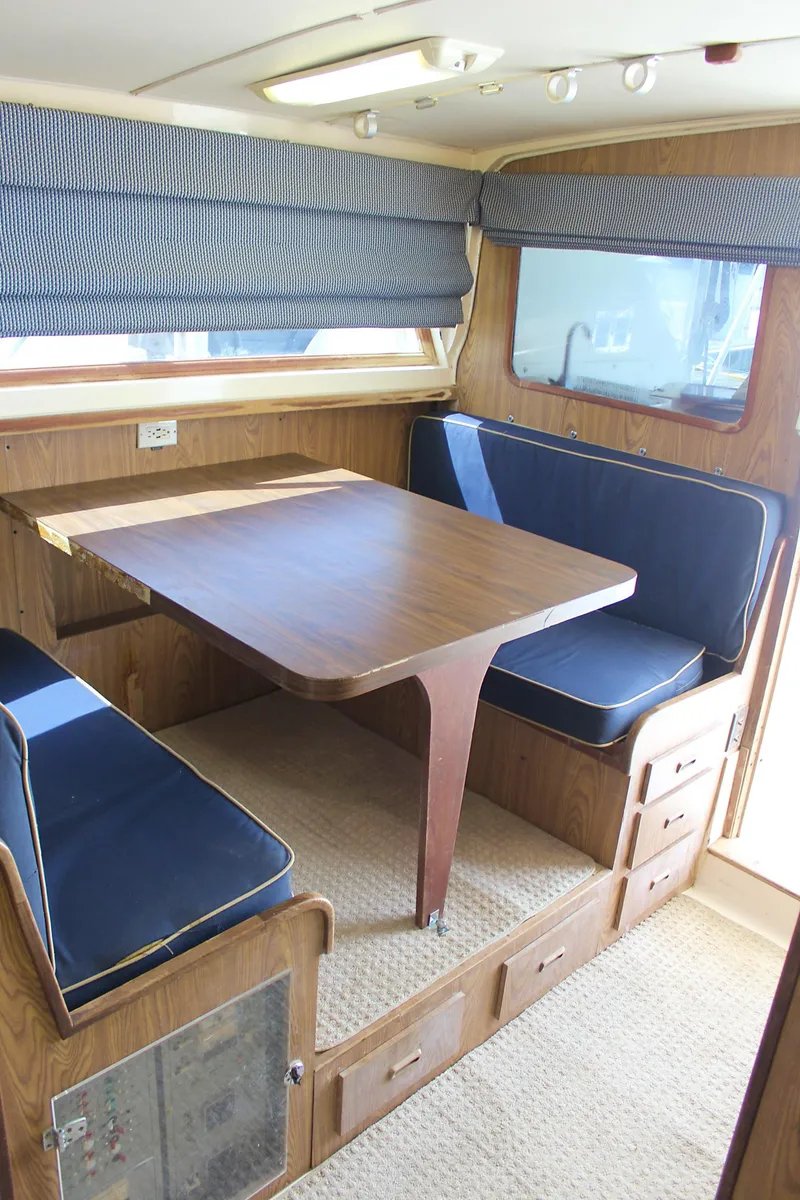 Slide: The Image of 1980 Bertram Sport Fisherman interior with wooden dining table and blue cushioned seating. - 18