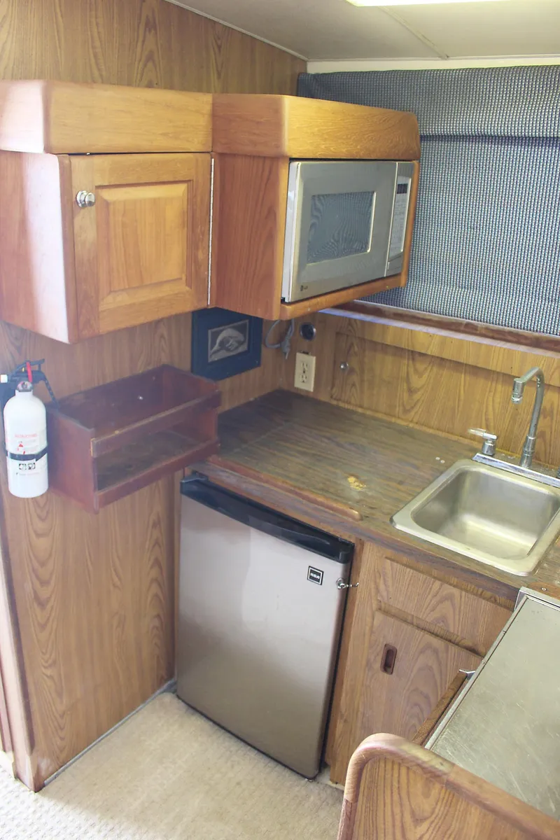 Slide: The Image of 1980 Bertram Sport Fisherman boat kitchen with wood cabinets, microwave, mini-fridge, and sink. - 20