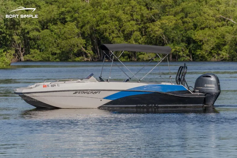 Slide: The Image of 2023 Starcraft SVX 211 OB boat on calm water with lush green background. - 0