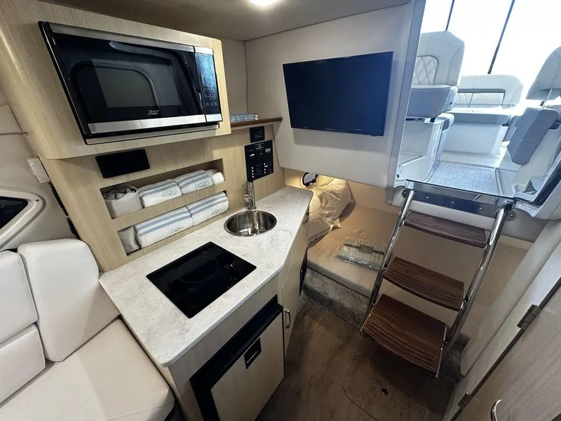 Slide: The Image of 2024 Regal 26XO boat interior with kitchenette, TV, and ladder to upper deck. - 13