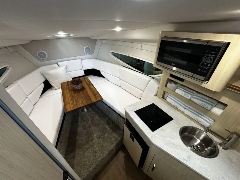 Slide: The Image of Interior of 2024 Regal 26XO boat with white seating, wooden table, and kitchenette. - 16