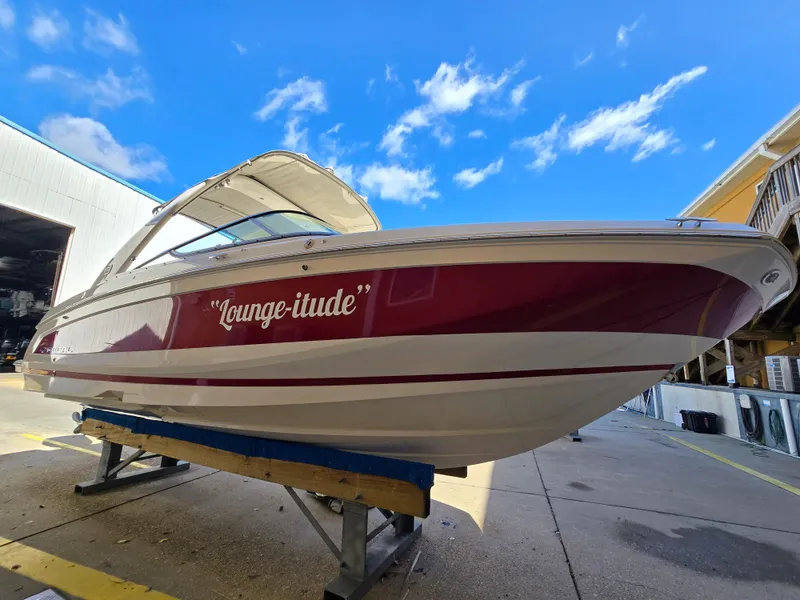 Slide: The Image of 2019 Regal 26 OBX boat named "Lounge-itude" on a stand under blue sky. - 26