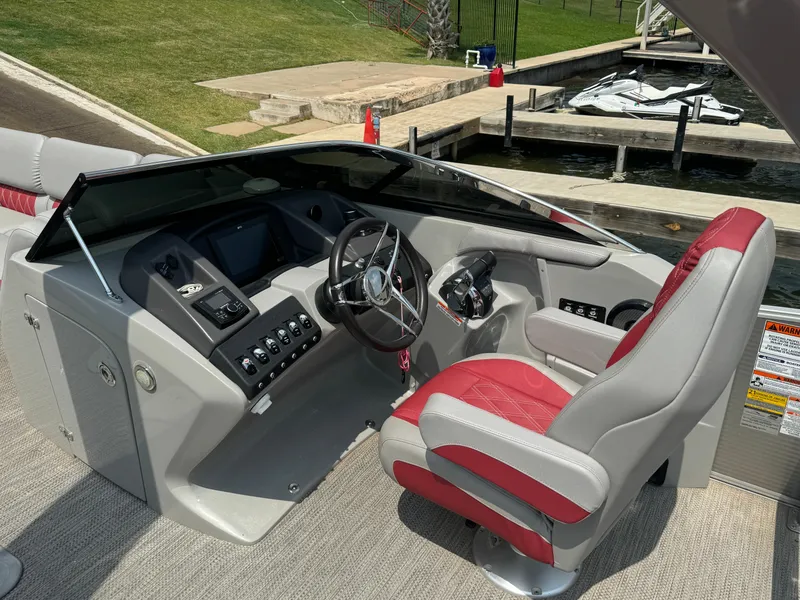 Slide: The Image of 2020 Bennington QSBWAX2SG boat cockpit with red and gray captain's chair, docked by the water. - 9