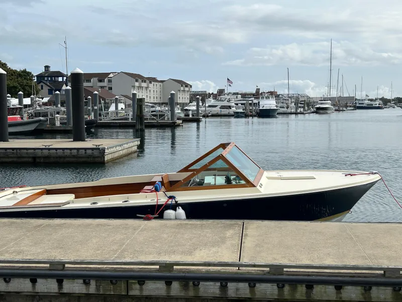 Slide: The Image of 1972 Bertram 25 boat docked at a marina with waterfront buildings in the background. - 6