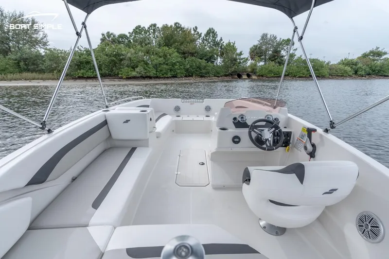 Slide: The Image of 2022 Starcraft SVX 171 OB boat interior with seating and steering wheel, docked near a lush shoreline. - 4