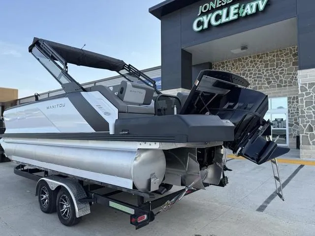 Slide: The Image of 2024 Manitou Cruise 22 Max Bench V-Toon boat on trailer outside dealership. - 3