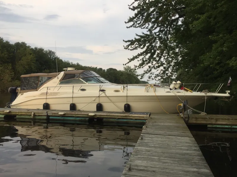 The Image of 1995 Sea Ray 450 Sundancer yacht docked by a wooden pier, surrounded by trees. - 0