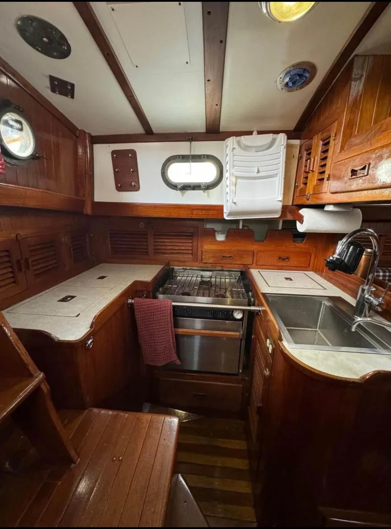 Slide: The Image of 1977 Tayana 37 yacht kitchen with wood cabinetry, stove, and sink. Cozy maritime design. - 6
