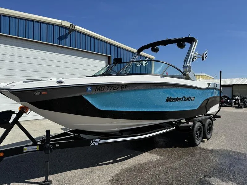 Slide: The Image of 2022 MasterCraft XT24 boat on trailer outside blue warehouse. - 1