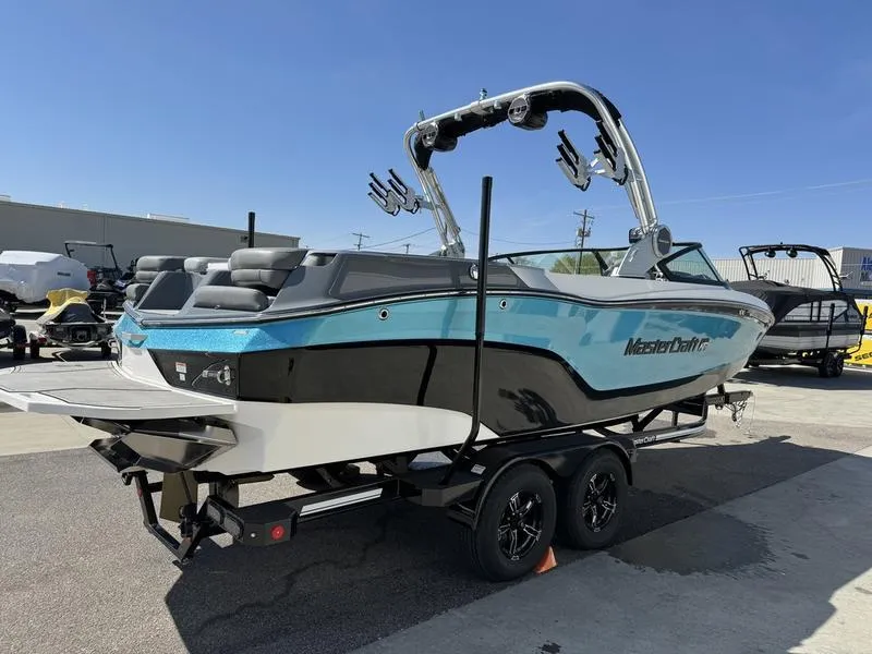 Slide: The Image of 2022 MasterCraft XT24 boat on trailer, blue and black exterior, parked outdoors. - 2