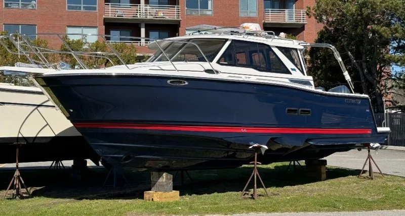 Slide: The Image of 2024 Cutwater C-288 C LE boat on stands, blue hull with red stripe, docked near buildings. - 1