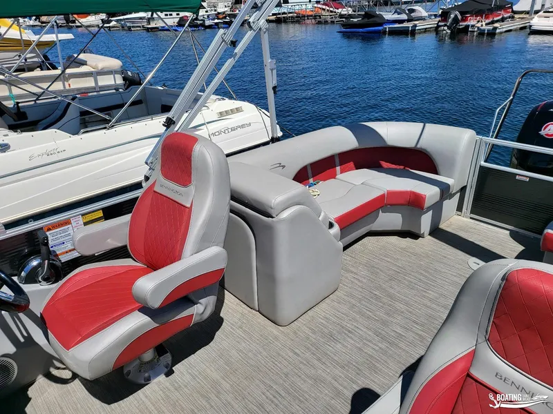 Slide: The Image of 2021 Bennington L25 Stern Radius pontoon boat interior with red and gray seating at marina. - 11